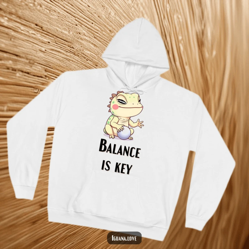 Funny Winking Iguana Hoodie, balancing a ball with a cheeky wink, exuding humor and a playful, mischievous personality.